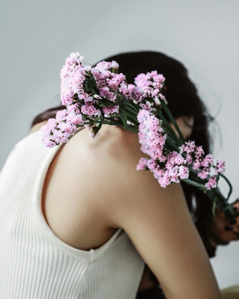Mujer con ramo de flores lilas en actitud introspectiva, simbolizando vulnerabilidad y búsqueda de autoestima.